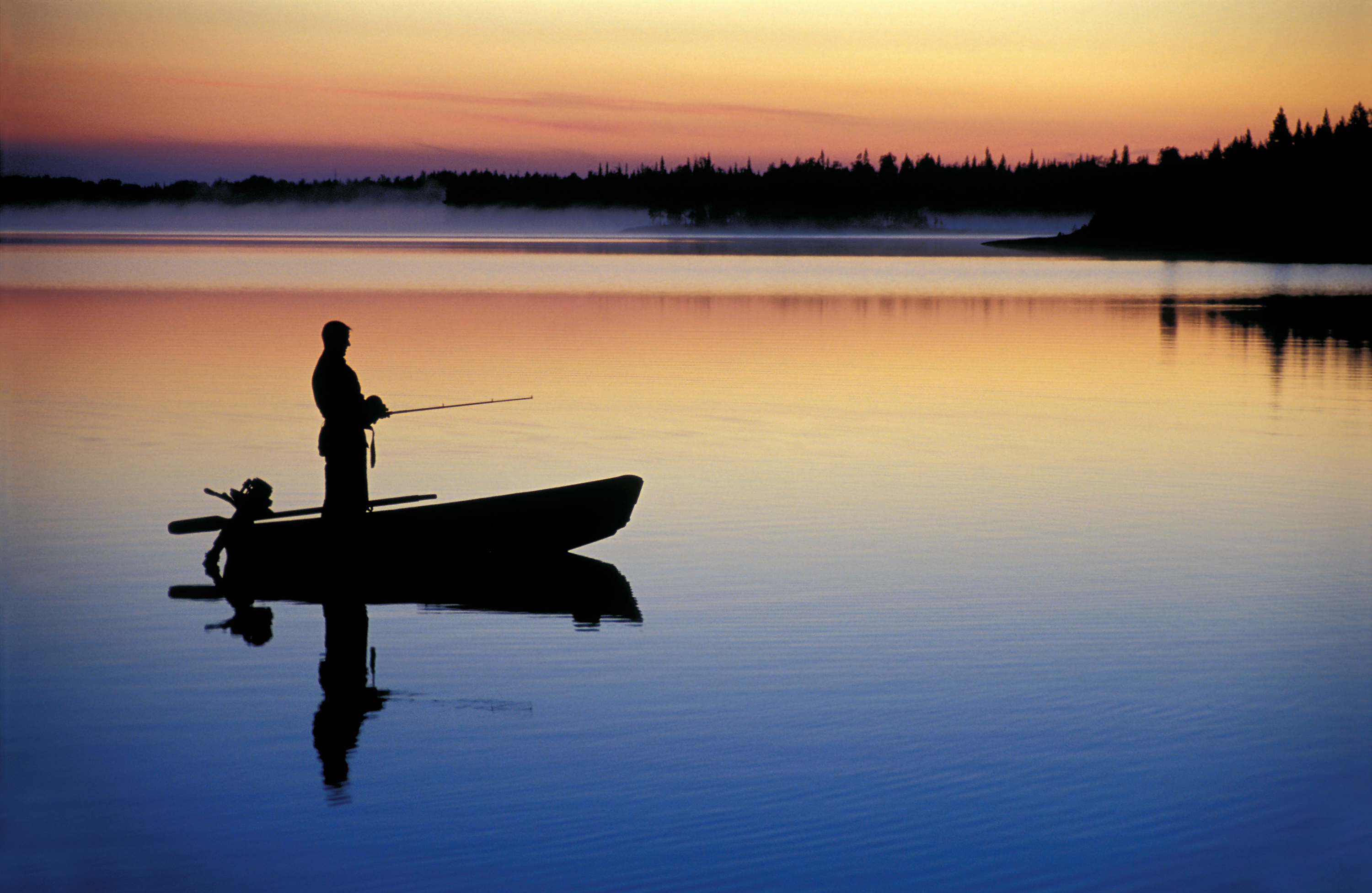Silhouette of a person fishing from a boat on the water. 