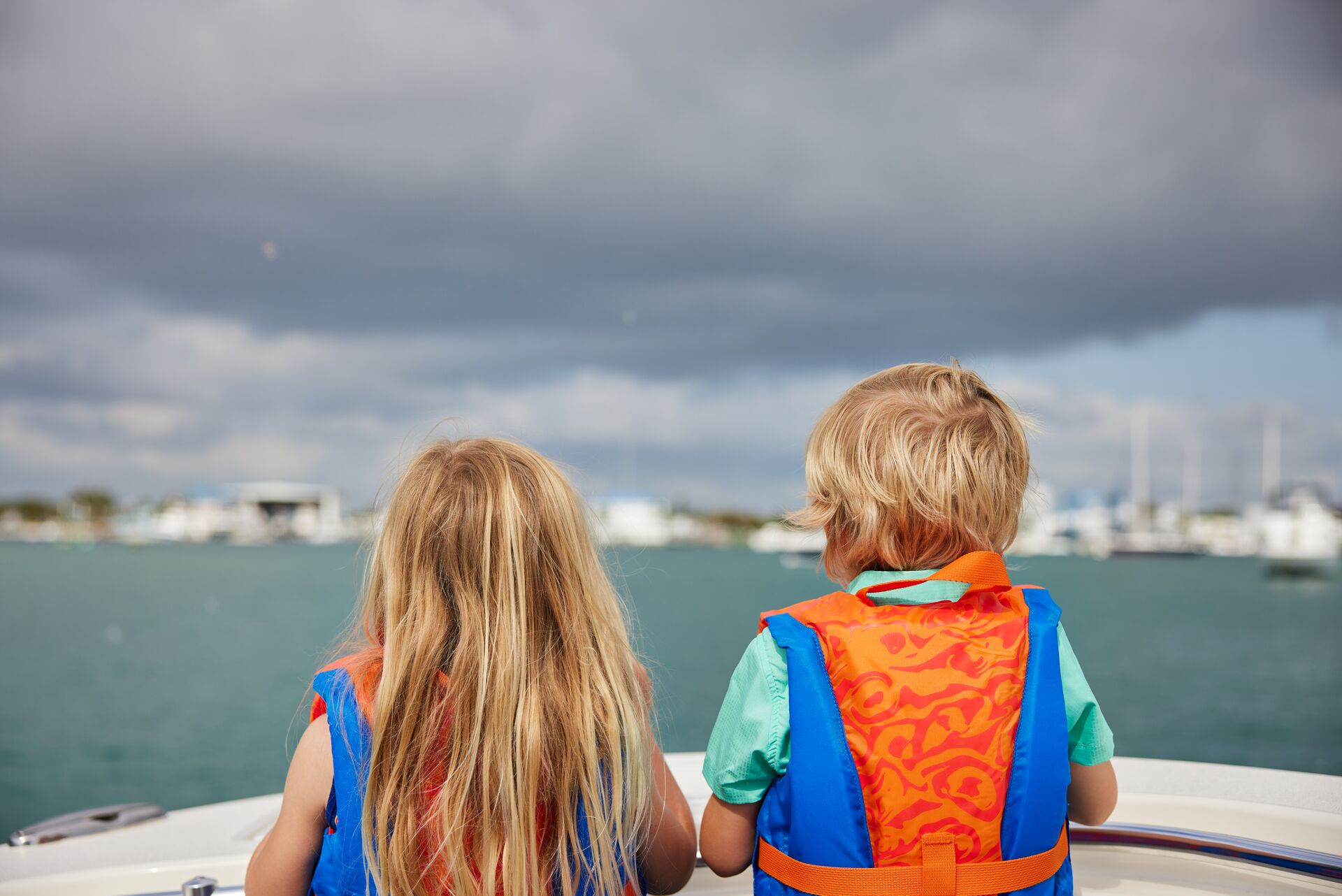 Two children in lifejackets facing the back of a boat, be aware of rip currents concept. 