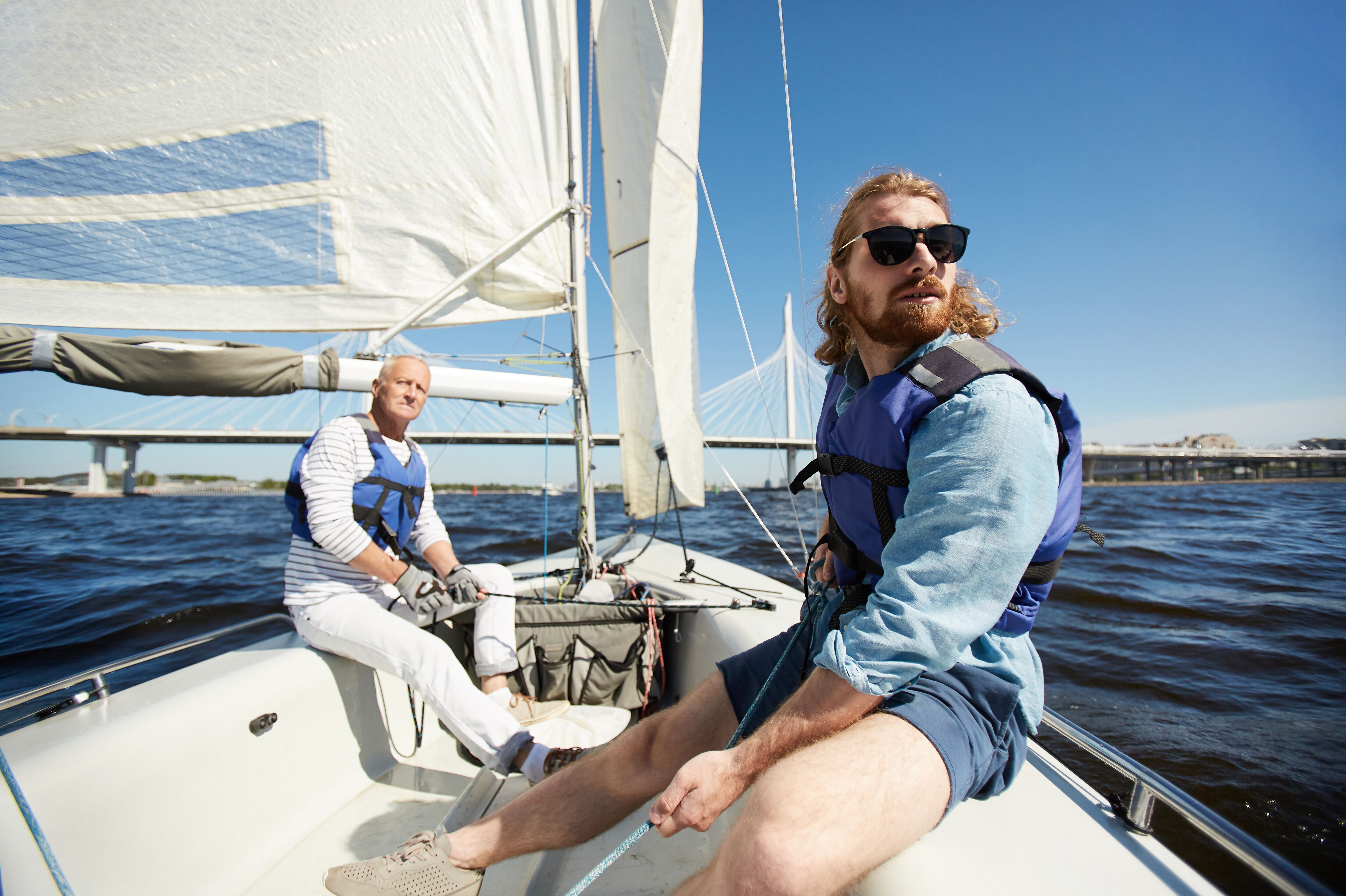 Two men operating a sailboat on the water. 