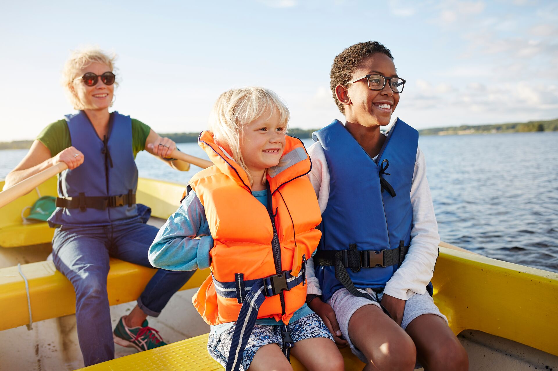 A woman paddling a boat with two kids, lifejackets for canoe concept. 