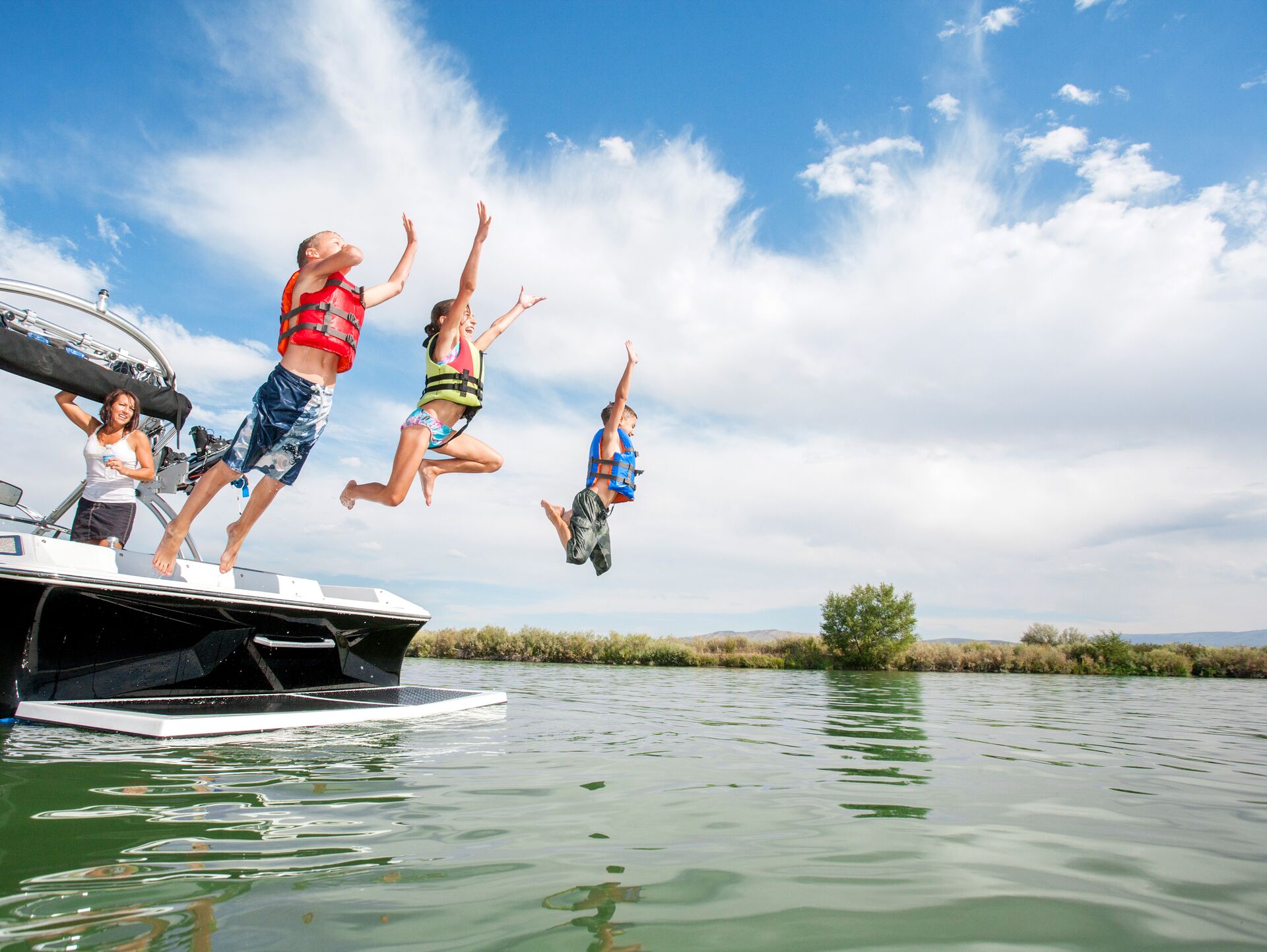 Children wearing lifejackets jumping into the water from a boat, surroundings for skiing and watersports safety concept. 