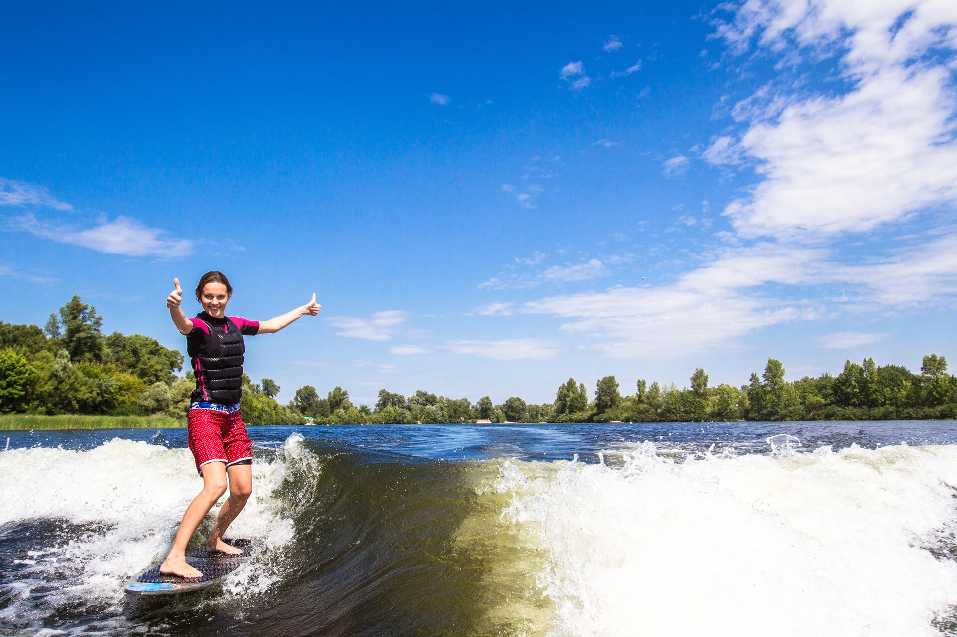 A girl wearing a lifejacket on a wakeboard behind a boat, skiing and watersports safety. 