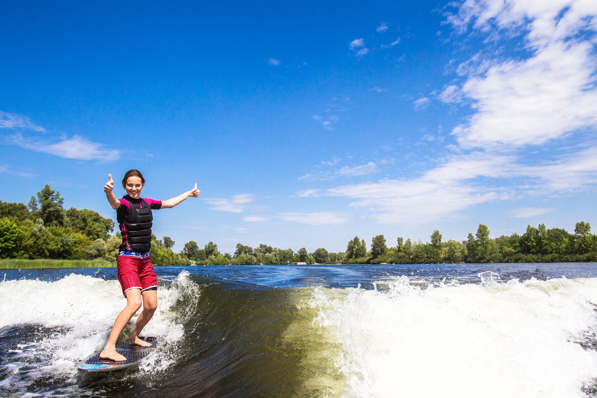A person holds thumbs up while wake surfing behind a boat, staying safe concept. 