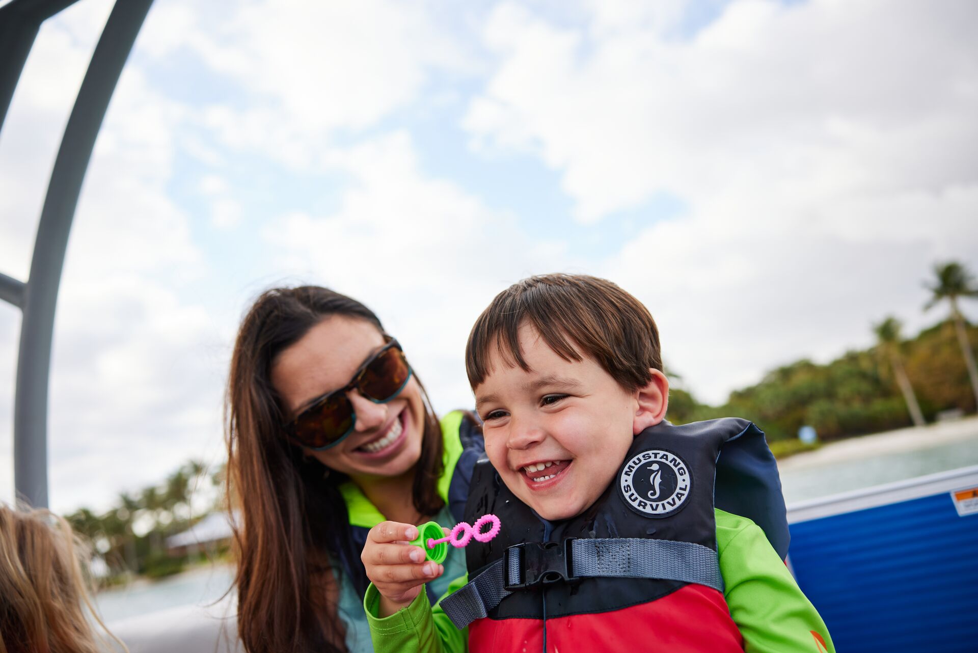 A smiling woman with child blowing bubbles wearing lifejackets on a boat, boat motors and safety concept. 