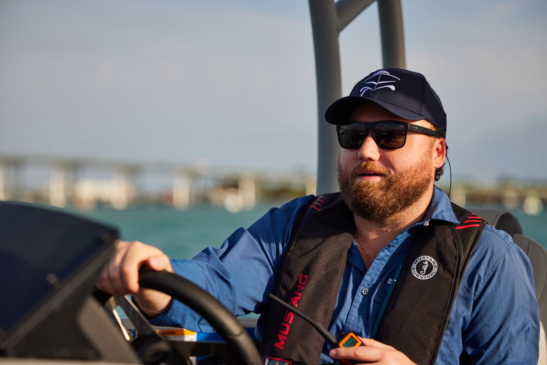 A man smiling while wearing a lifejacket and driving a boat, represents boat safety. 