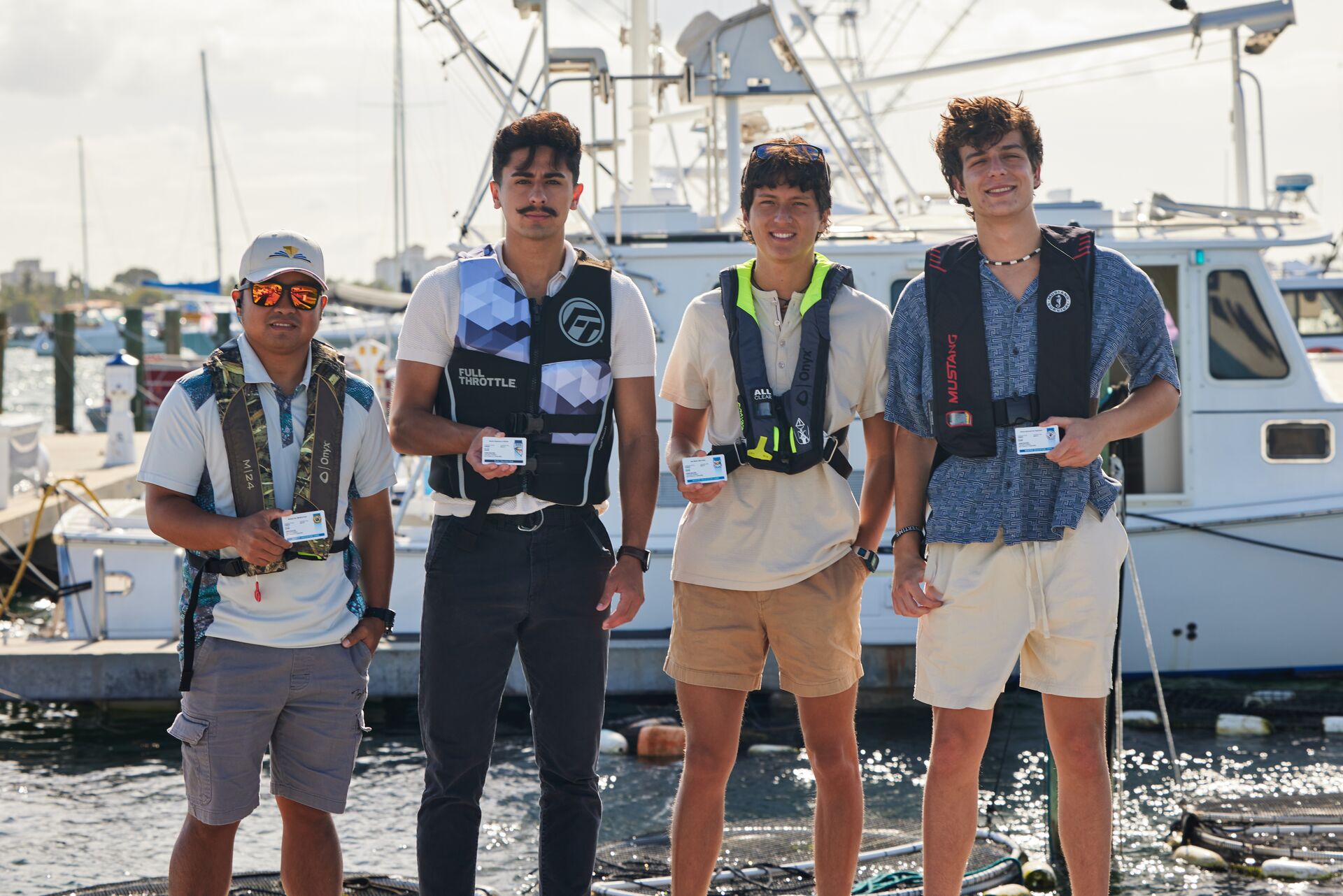 Four men wearing lifejackets and smiling while holding boating license cards. 