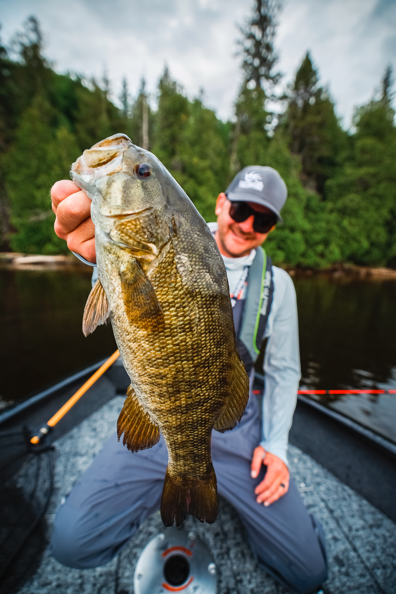 A man holds up a freshly caught bass while in a boat. 