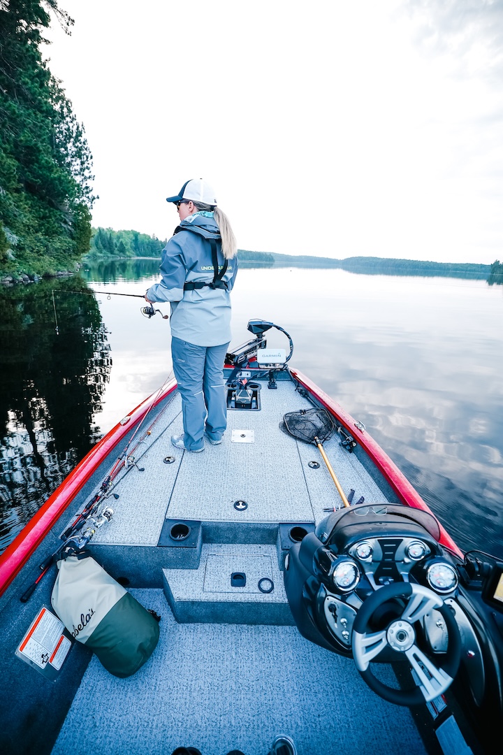 A woman stands at the front of a boat while fishing. 