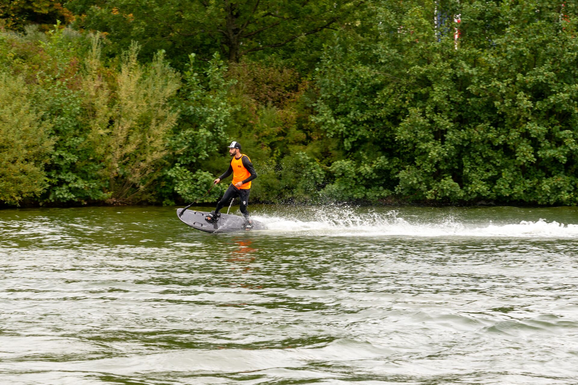 A guy rides a motorized surfboard on the water. 