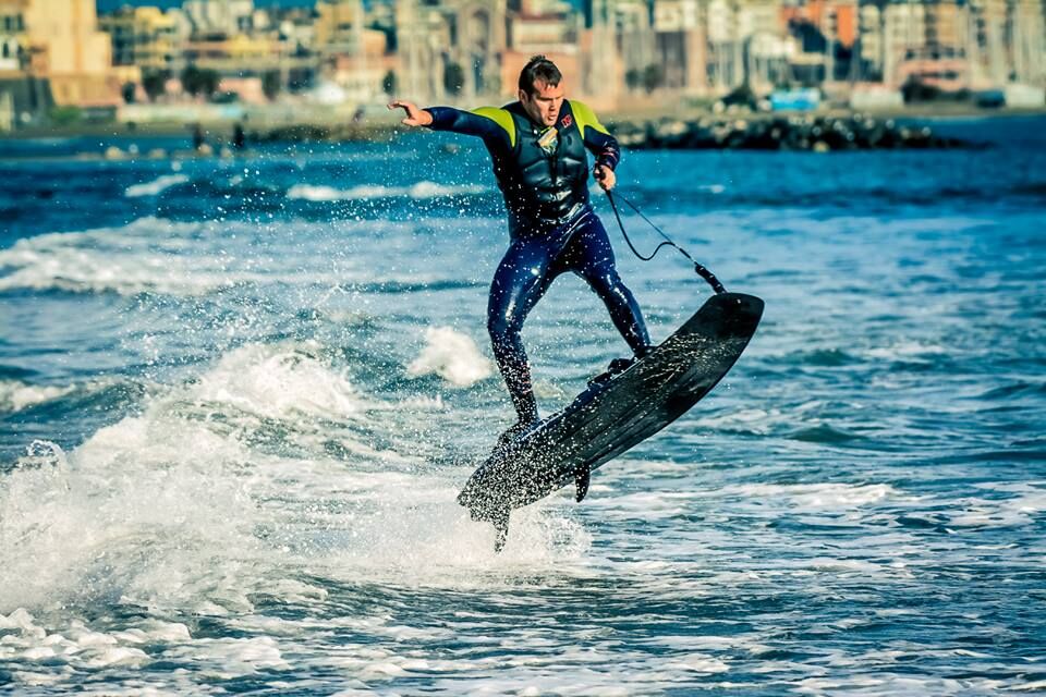 A man in a wetsuit on a motorized surfboard on the water.