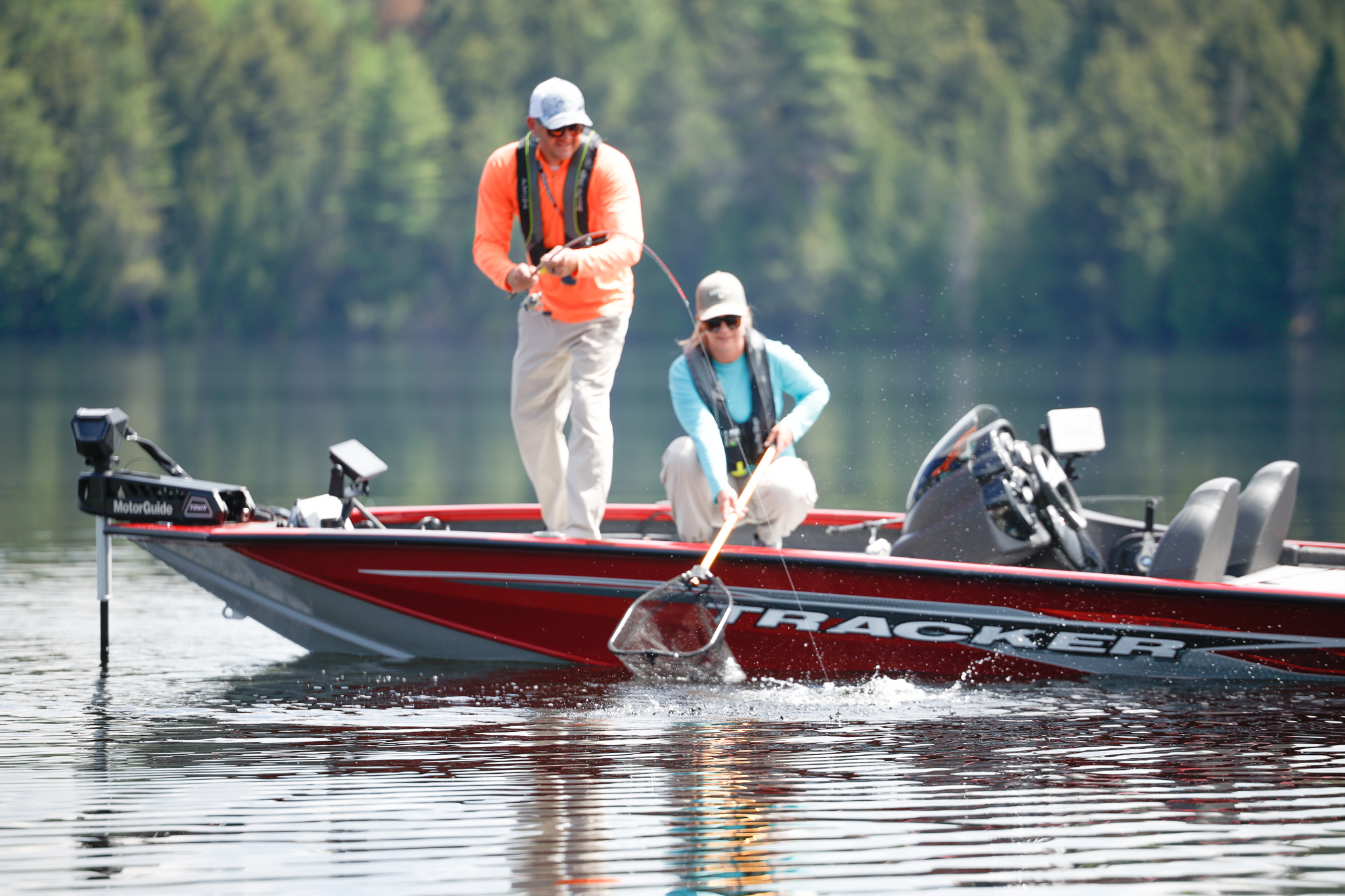 Two people on a fishing boat reeling in a fish from the water. 