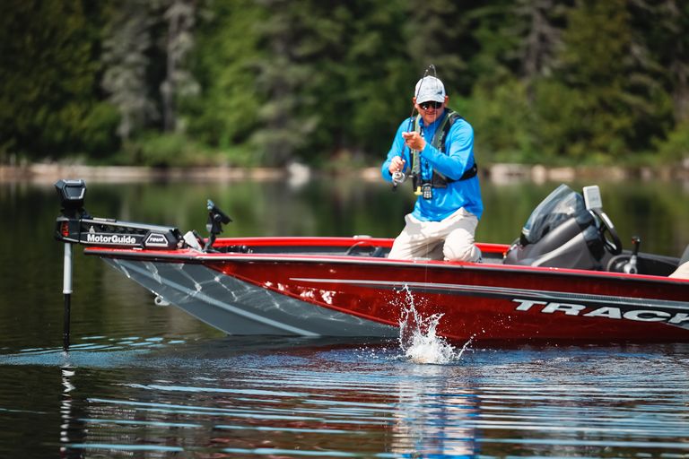 An angler reels a fish onto a boat, spotted bass vs. largemouth bass concept. 