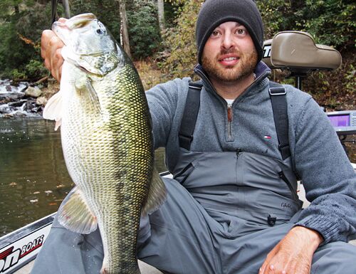 A man holds up a spotted bass after a catch. 