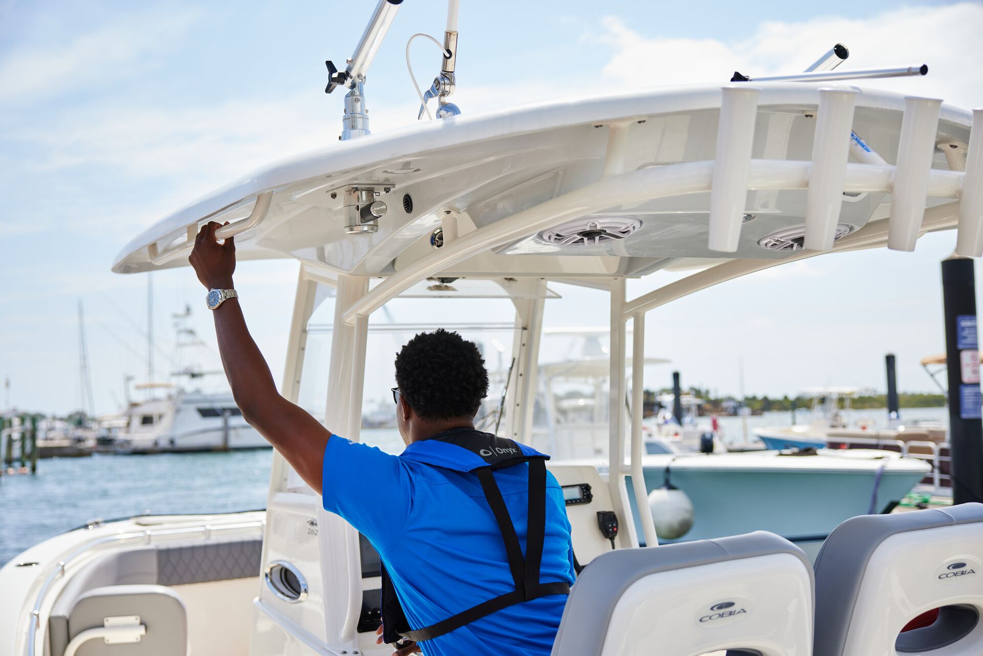 A man in a blue shirt and life vest drives a boat, captain's license Canada concept. 