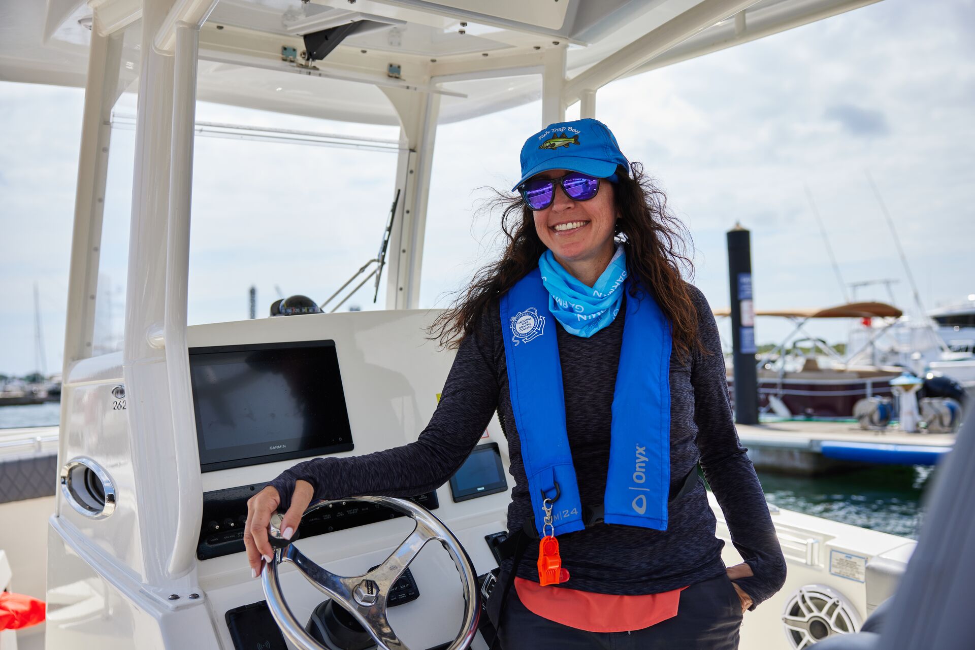 A woman smiles at the helm of a boat while wearing a blue life vest. 