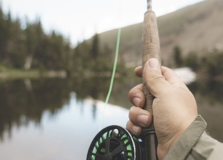 A hand holding a fly fishing pole over the water.