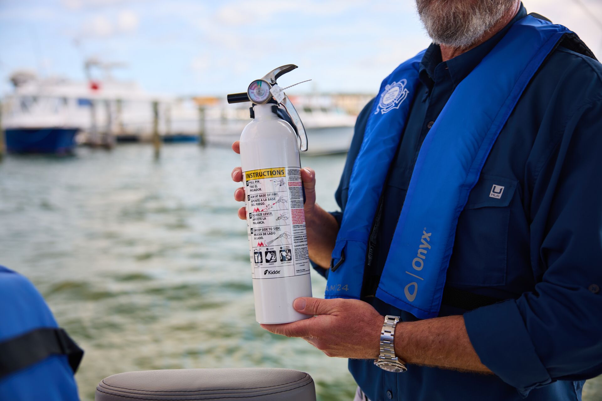 A man in a life jacket holds a fire extinguisher on a boat.