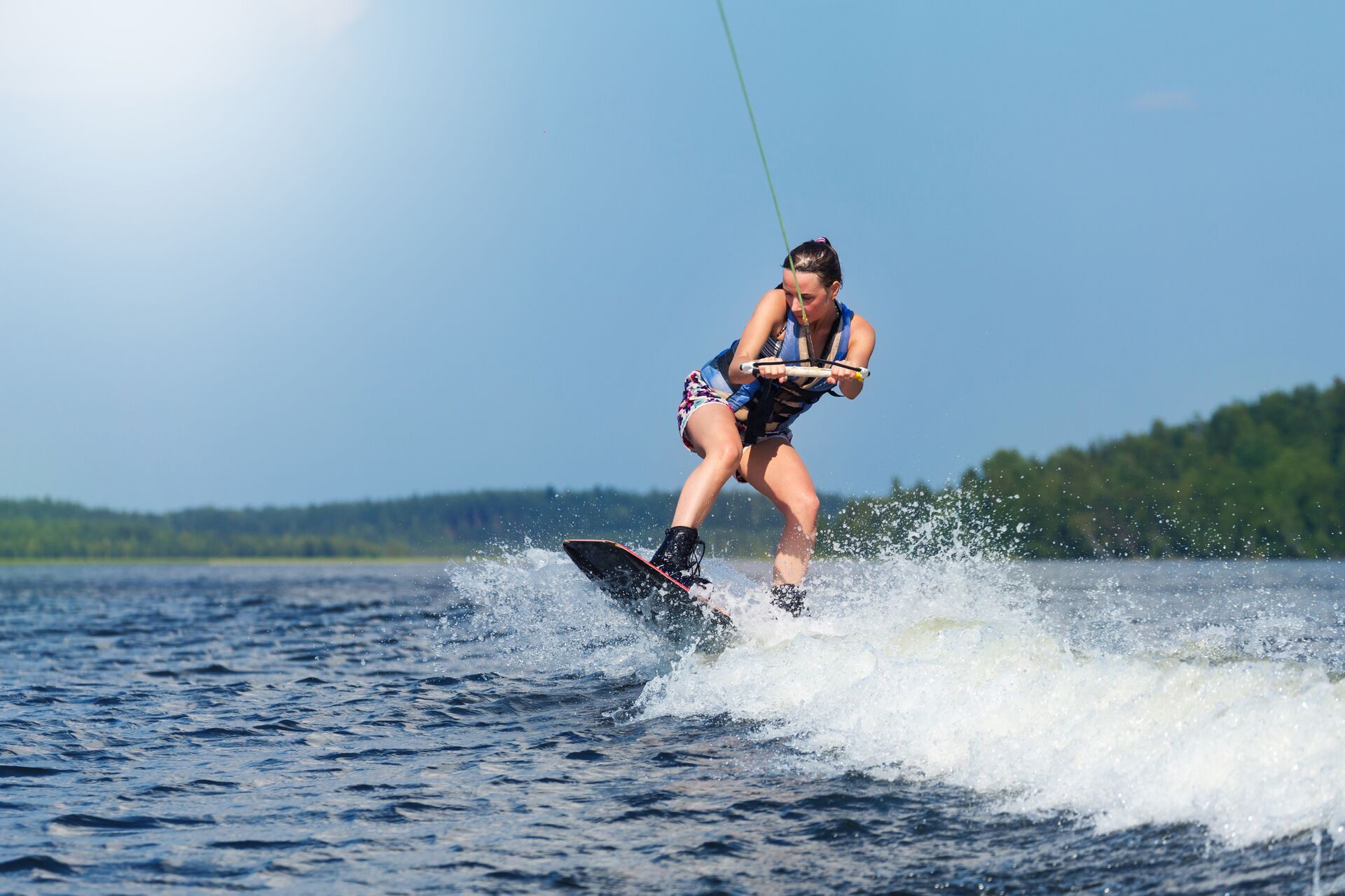 A girl on a wakeboard while holding a rope and being towed behind a boat. 