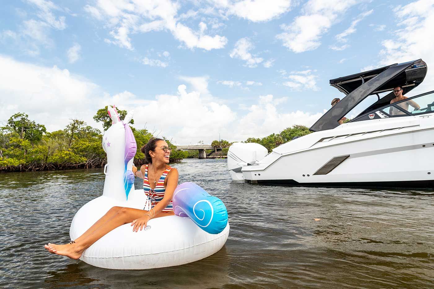 A girl smiling and sitting on a unicorn inflatable near a boat propeller. 