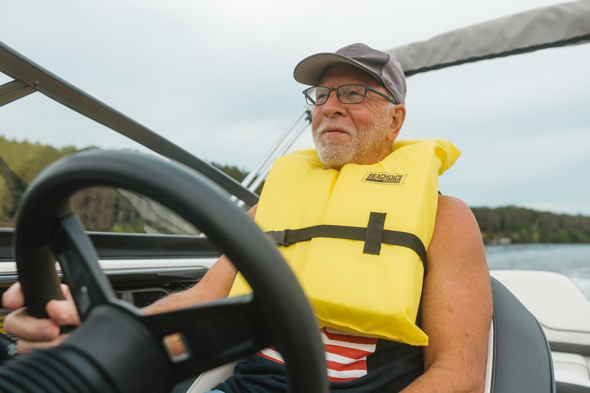 A man smiles while wearing a yellow life vest and driving a boat. 